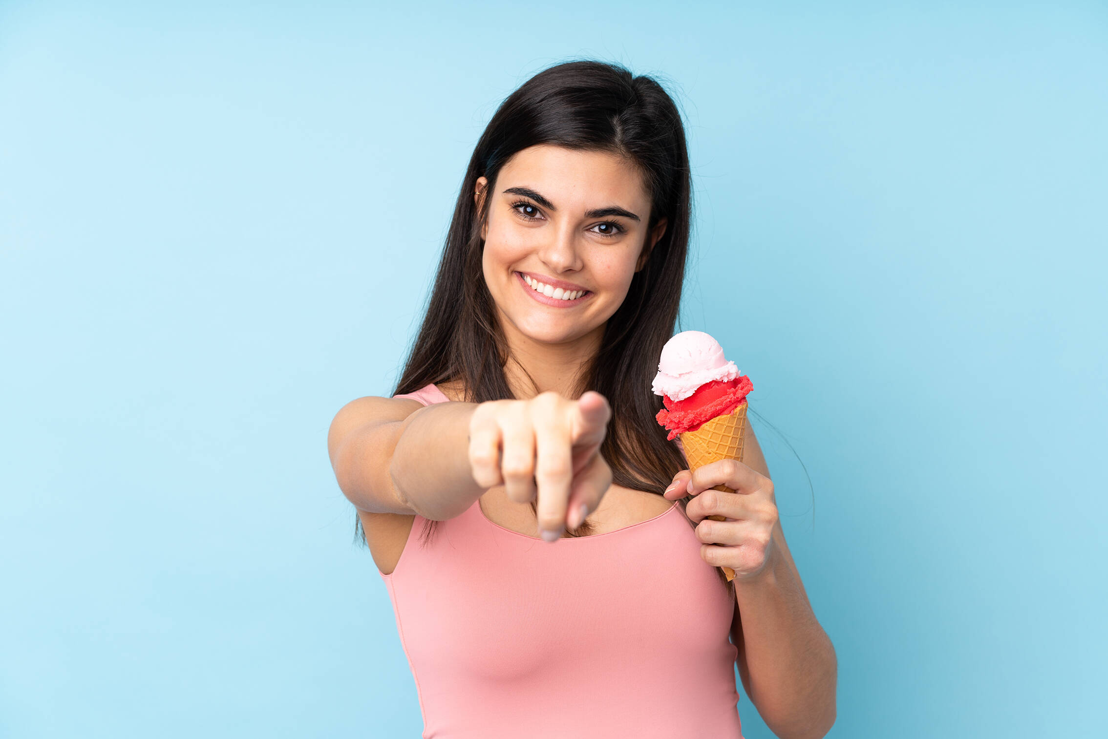 Young woman holding cornet ice cream blue wall points finger you with confident expression